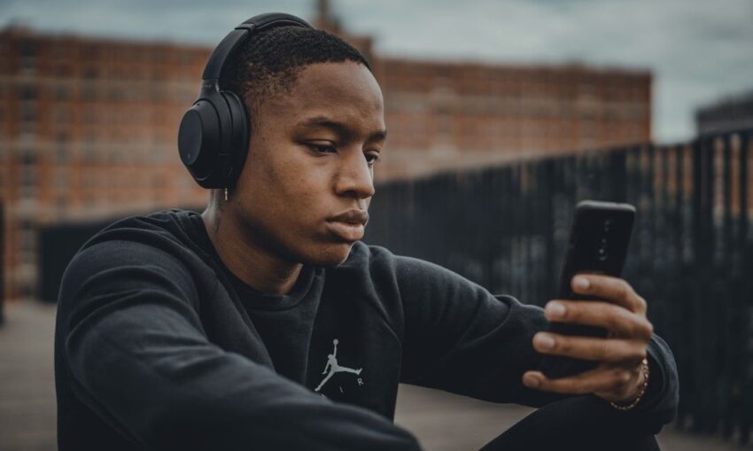 Person med hörlurar tittar på en smartphone utomhus